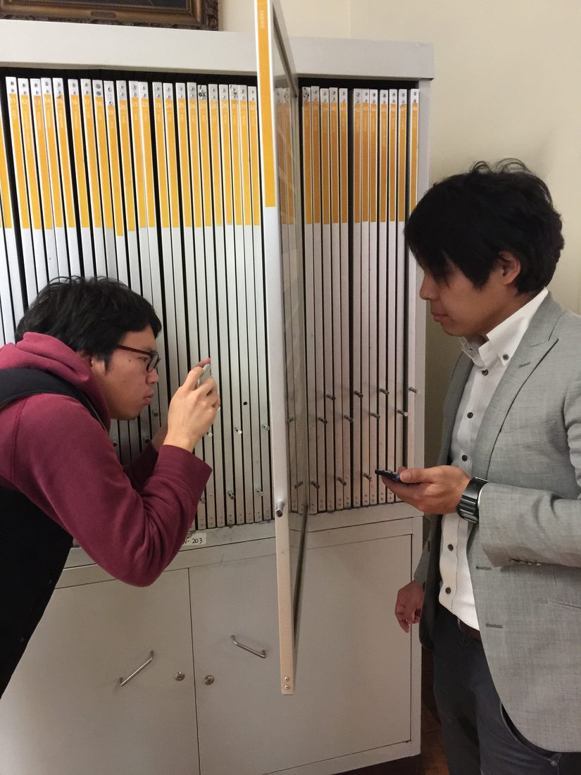 Two Japanese students examining stamp display panels at a post office in Santiago