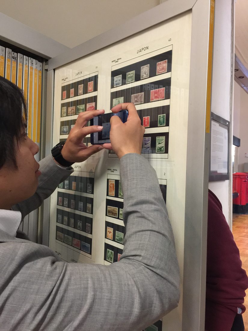 A student photographing a display panel of Japanese stamps at a post office in Santiago