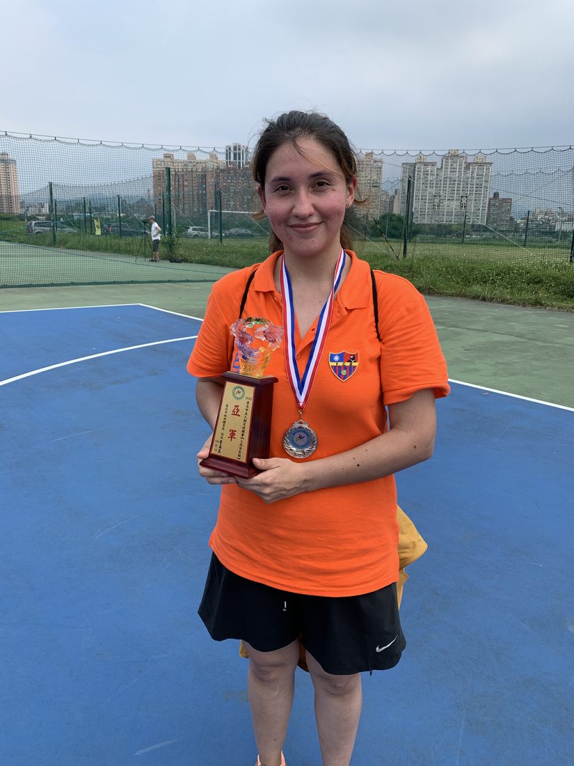 Paulina in a coaching shirt holding a medal and trophy on a pitch